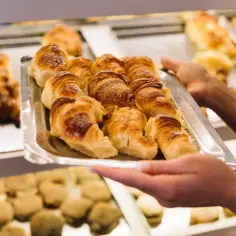 Taca z croissantami w piekarni, trzymana przez ręce.